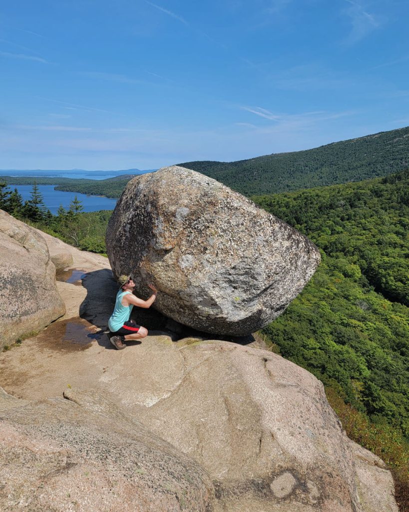 Hiker pretending to try to push Bubble Rock off the edge at on South Bubble Trail of Acadia National Park in Maine 