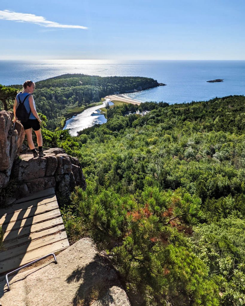 Hiker on boardwalk section of Beehive Trail overlooking Sand Beach in Acadia National Park in Maine