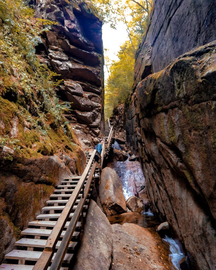 Woman smiles and leans over stairs of Flume Gorge boardwalk in the White Mountains of New Hampshire in fall